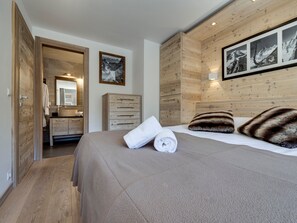 Ein Hotelzimmer mit einem hölzernen Kopfteil, einem großen Bett mit einem weißen Handtuch aufgerollt, einer Holzkommode und einem Spiegel.