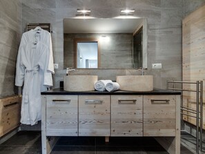 Ein modernes Badezimmer mit einem Holzbadezimmer-Möbel, zwei Waschbecken, einem großen Spiegel und einem Bademantel an einem Haken.