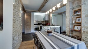 Une cuisine moderne avec des meubles blancs, un îlot central et un coin repas agrémenté d’une nappe à rayures et de chaises.