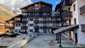 A multi-story hotel with balconies, stone walls, and a mountainous backdrop. - Renovated apartment near slopes - 5 guests (Val-d'Isère)