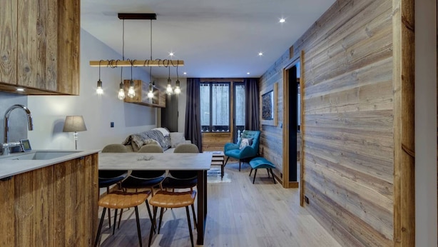 A modern kitchen with wooden accents, a dining area with a table and chairs, and a cozy seating area with a blue armchair. - Renovated apartment near slopes - 5 guests (Val-d'Isère)