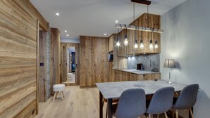 A modern kitchen with wooden accents, a dining area with four chairs, and a visible bathroom in the background. - Renovated apartment near slopes - 5 guests (Val-d'Isère)