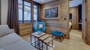 A modern living room with wooden panel walls, a large window, a sofa, a blue armchair, and a small table. - Renovated apartment near slopes - 5 guests (Val-d'Isère)