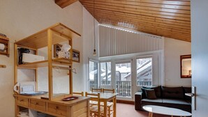 Tunnelmallinen huone, jossa on puinen pöytä ja tuolit, sohva sekä suuret ikkunat, joista avautuu näkymä lumipeitteisiin rakennuksiin.
