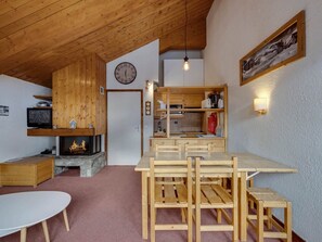 A cozy cabin interior with a wooden dining table, chairs, a fireplace, a kitchen area, and a clock on the wall. - Apartment 5 guests, clear view, at the slopes (Val-d'Isère)