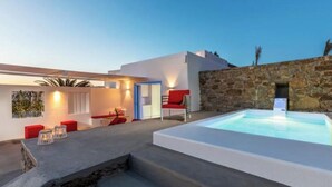 A modern outdoor pool area with a stone wall, a red chair, and a small table. - o Lofos CHORA Deluxe Suite with Private Pool (Mykonos)