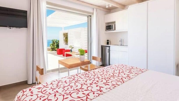 A bedroom with a bed, a TV, a kitchenette, and a view of the outdoors. - o Lofos CHORA Deluxe Suite with Private Pool (Mykonos)