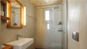 Casa de banho com lavatório, espelho, chuveiro e sanita.