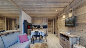 Ein modernes Interieur mit Holzbalkendecke, einem Essbereich mit Tisch und Stühlen, einem Sofa mit rosa Kissen sowie einem an der Wand montierten Fernseher.