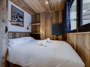 Quarto no estilo de cabana de madeira com uma cama, uma TV montada e um quadro na parede.