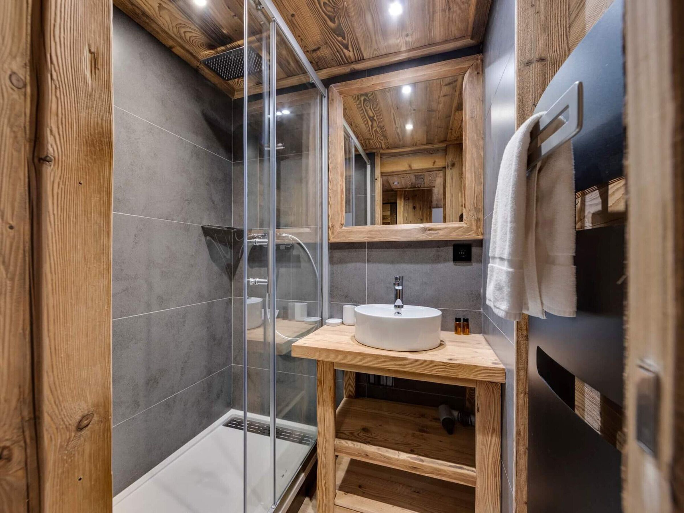 Ein modernes Badezimmer mit Duschkabine aus Glas, Waschtisch aus Holz und großem Spiegel.