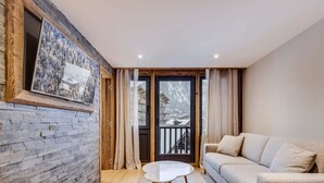 Ein gemütliches Wohnzimmer mit Steinwand, Holzboden, rundem Tisch und beiger Couch.