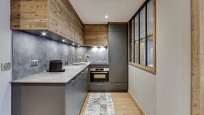 Eine kleine Küche mit grauen Schränken, einer Wand mit Holzvertäfelung, einer gefliesten Spritzschutzleiste und einem Fenster mit Holzrahmen.