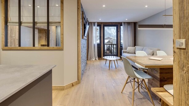 Eine moderne Küche mit Holzelementen, ein Essbereich mit Holztisch und -stühlen und ein Blick auf eine verschneite Landschaft durch große Fenster.
