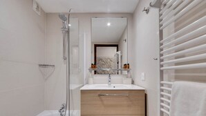 Ein modernes Badezimmer mit einer gläsernen Dusche, einem weißen Waschbecken mit Marmorplatte, Holzschränken und einem Handtuchhalter.