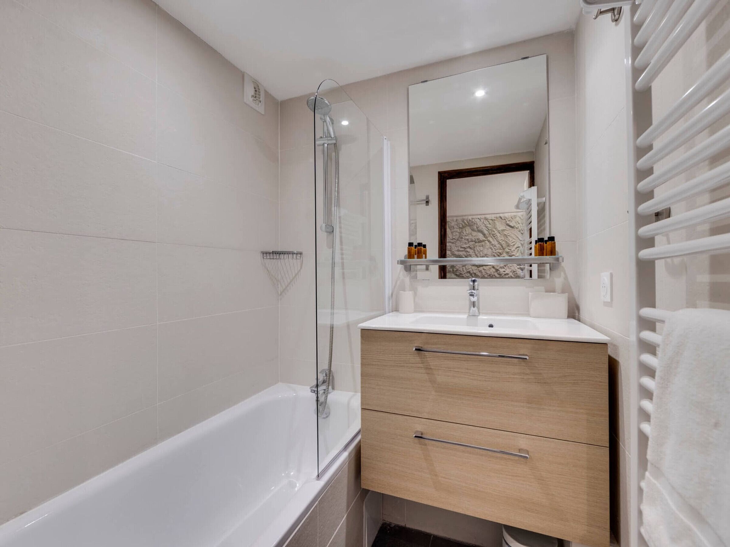 Une salle de bain moderne équipée d’une baignoire, d’une douche à parois de verre, d’un meuble-lavabo avec miroir et d’un porte-serviettes.