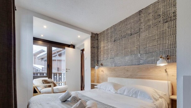 Ein modernes Hotelzimmer mit einem großen Bett, einem Holzkopfende und einem Balkon mit Blick.