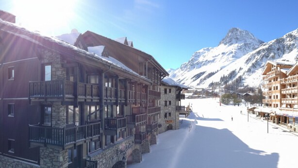 A snow-covered building with balconies and stone architecture, set against a backdrop of mountains and a clear sky. - Apartment with slope views, 6 guests (Val-d'Isère)