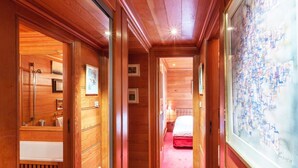 Een hal met houten lambrisering, een badkamer met douche en wastafel, en een bed in de verte.