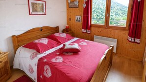 A wooden-paneled bedroom with a bed, a nightstand, a heater, a window with curtains, and a framed picture on the wall. - Charming apartment - 6 guests Saint-Jean-de-Sixt (Saint-Jean-de-Sixt)