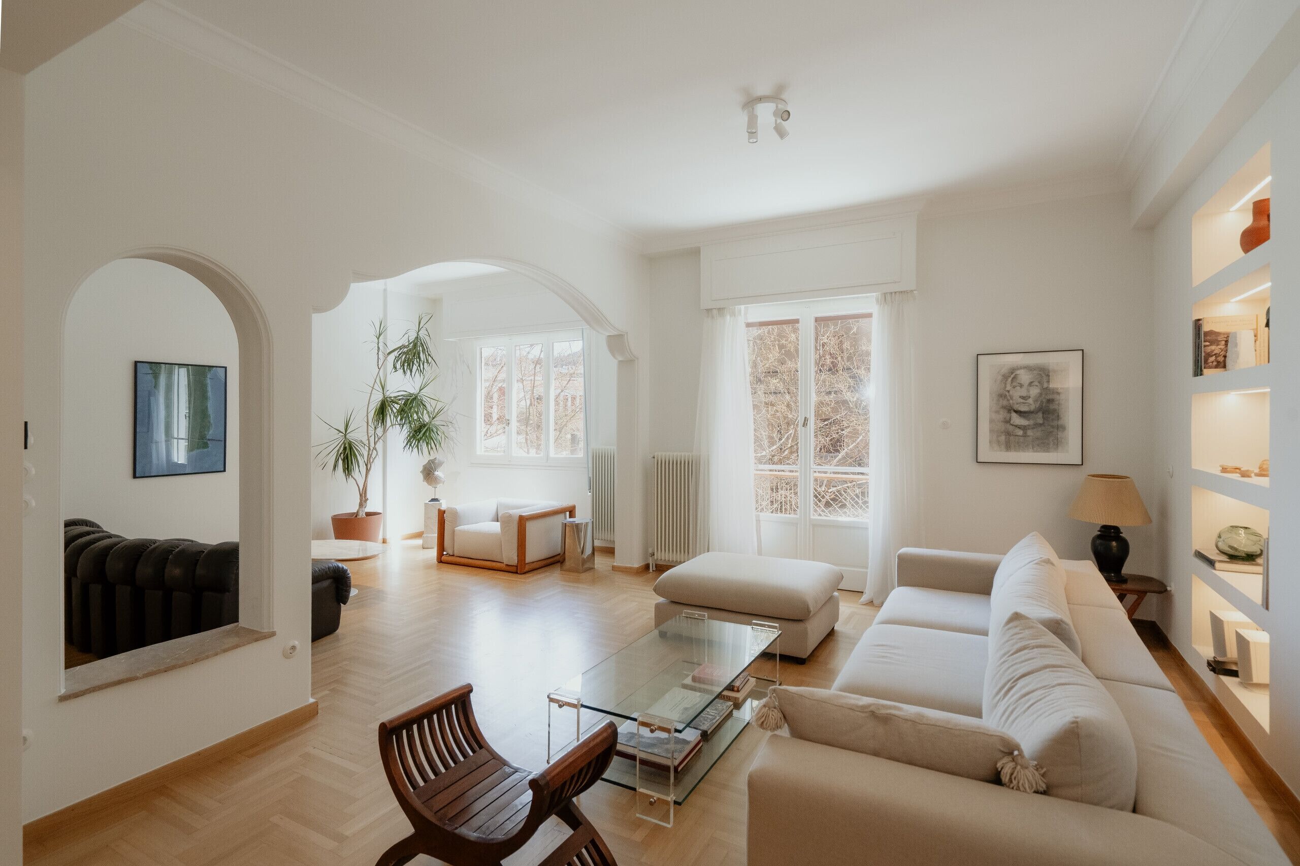 A spacious living room with a glass coffee table, a sofa, a chair, and a potted plant.