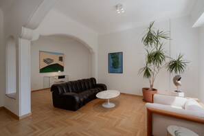 Ein modernes Wohnzimmer mit einer schwarzen Ledersofa, einem runden weißen Tisch, einer Topfpflanze und Kunstwerken an den Wänden.