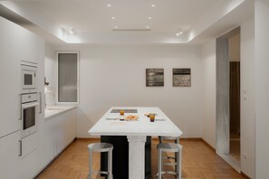 A compact kitchen with built-in appliances, a dining table with stools, and artwork on the walls. - Luxury 3BR & 3 Bathrooms Apt | Metro | By Museum (Athens)