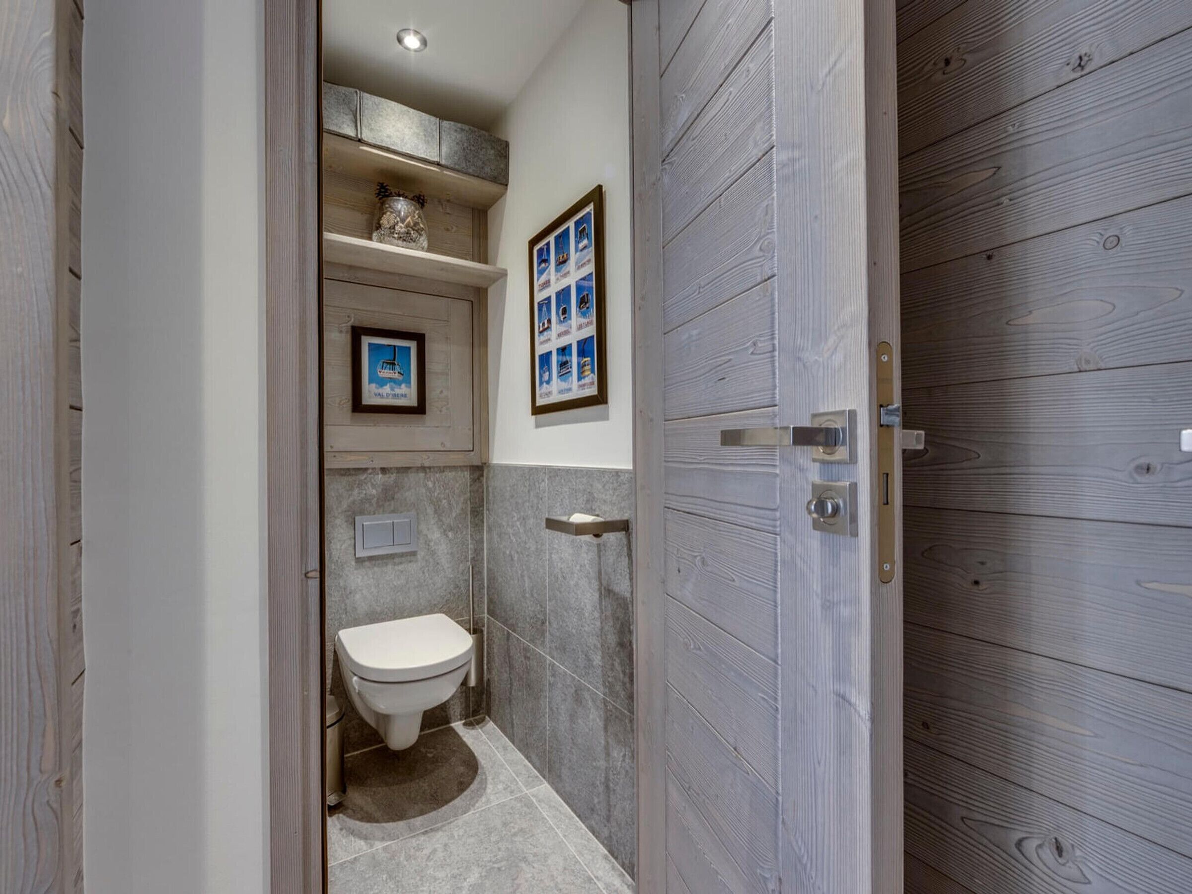 Un baño pequeño y moderno con inodoro, un estante con adornos y un cuadro en la pared.