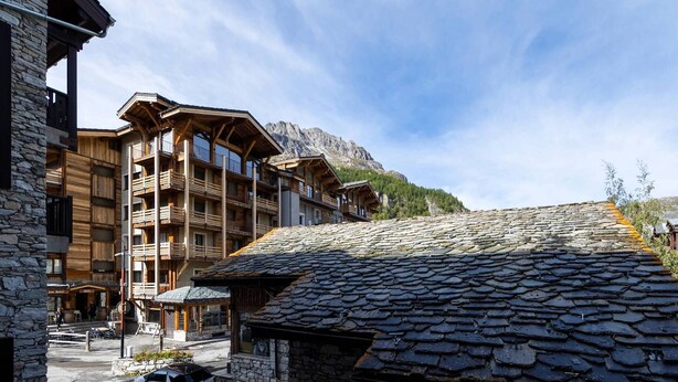 Edifici de fusta de diversos pisos amb balcons, parets de pedra i un paisatge de muntanya de fons.