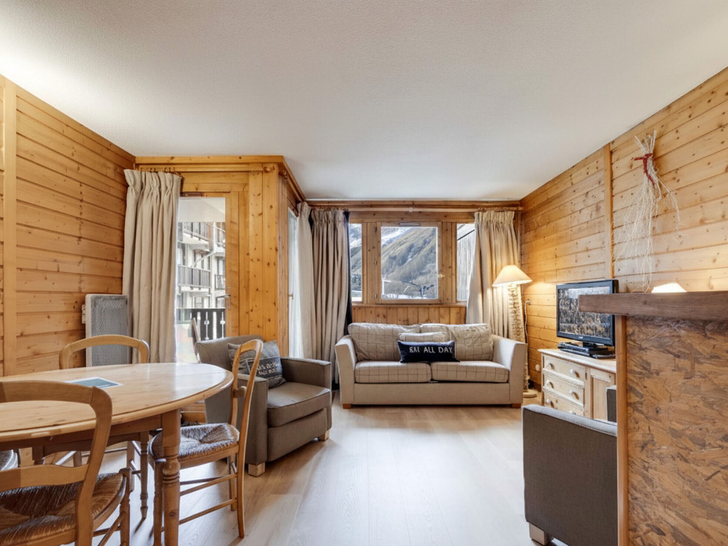 A cozy cabin interior with a wooden interior, a dining table with chairs, a sofa, and a television.