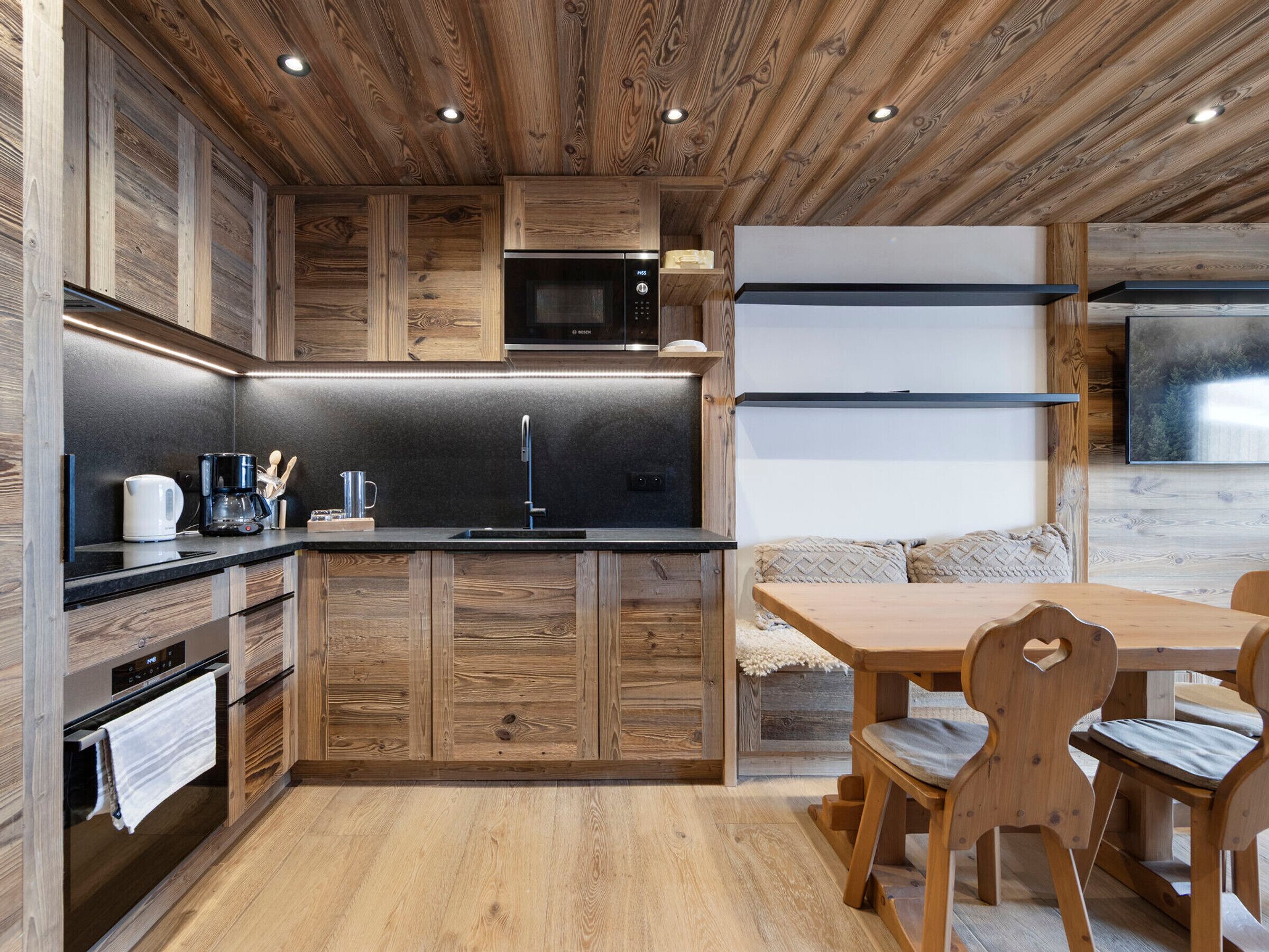A modern kitchen with wooden cabinetry, a black countertop, a Bosch microwave, and a dining area with a wooden table and chairs.