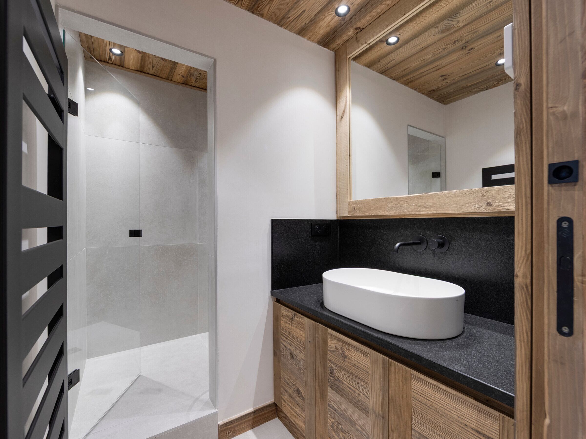 Een moderne badkamer met een houten plafond, een witte wastafel en een glazen douchecabine.