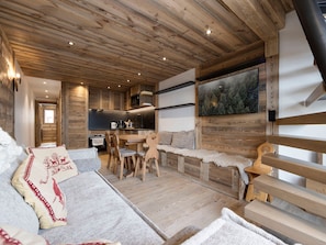 A cozy cabin interior with a wooden ceiling, a dining area, a sofa, and a painting of a forest. - Spacious apartment near slopes - 4 guests (Val-d'Isère)