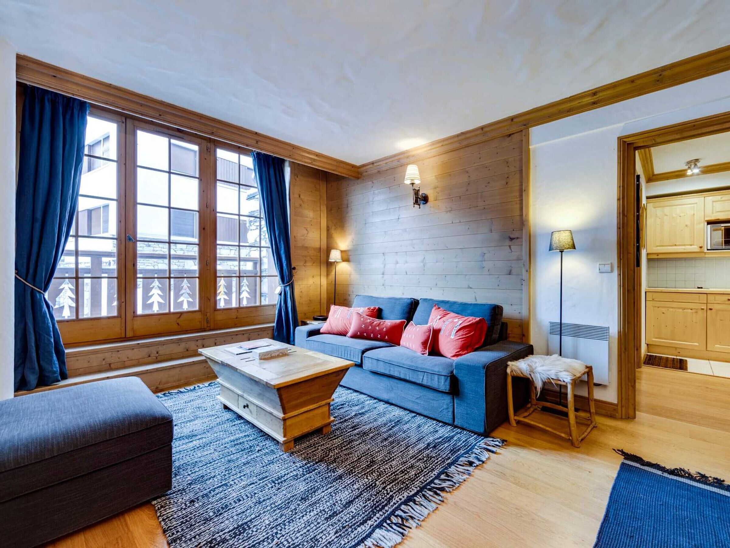 Una sala de estar acogedora con un sofá azul, una mesa de centro de madera y vistas al exterior a través de amplias ventanas.
