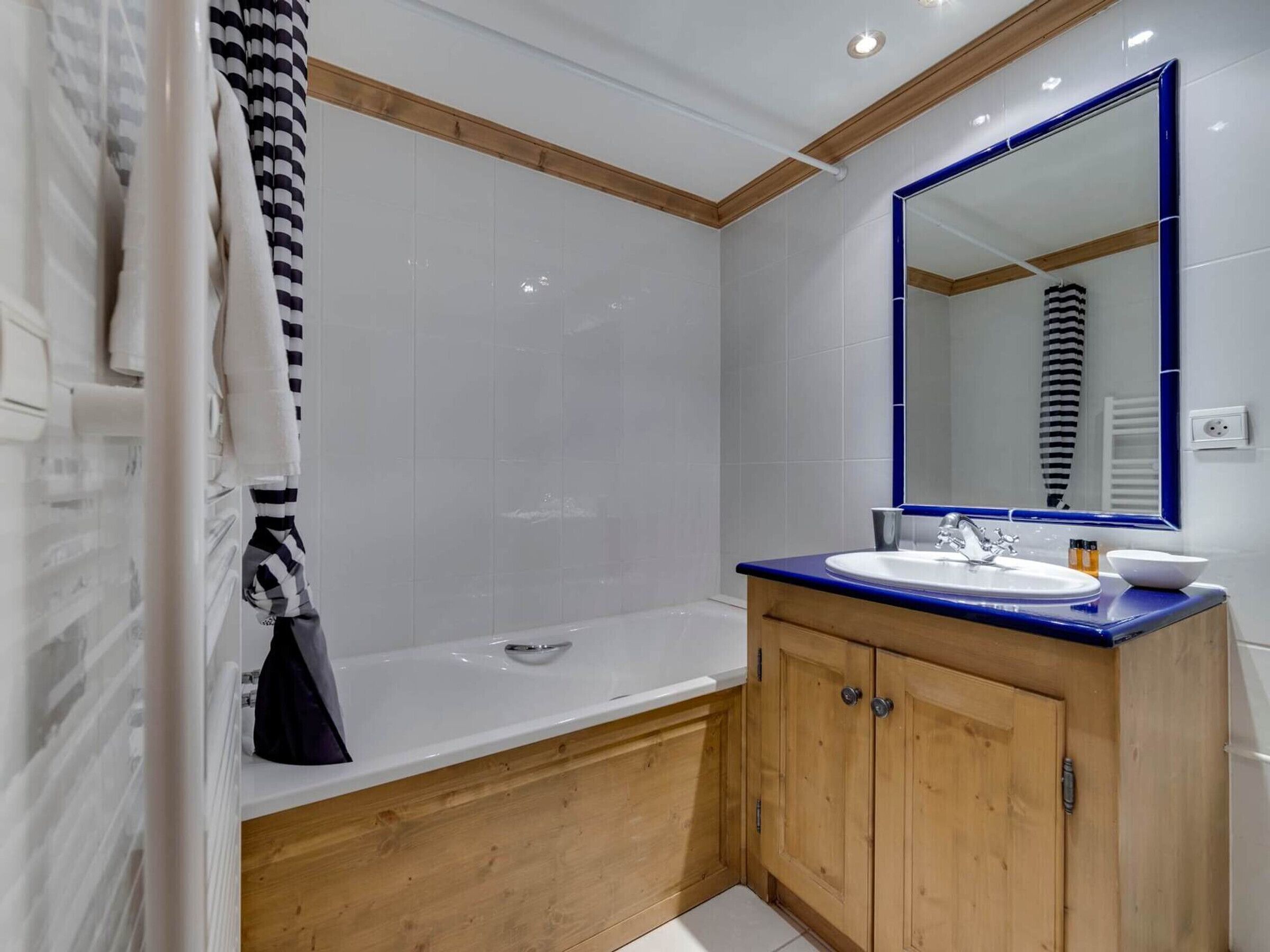 Un baño moderno con una bañera blanca, un tocador de madera con encimera azul y un espejo grande.