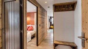 Habitació d'hotel moderna amb una porta de fusta, un llit amb roba de llit blanca i un coixí vermell, una banca de fusta i una taula petita.