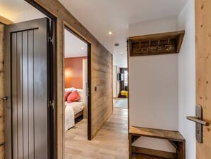 A modern hotel room with a wooden door, a bed with white bedding and a red pillow, a wooden bench, and a small table. - Ski-in apartment with parking - 5 guests (Val-d'Isère)