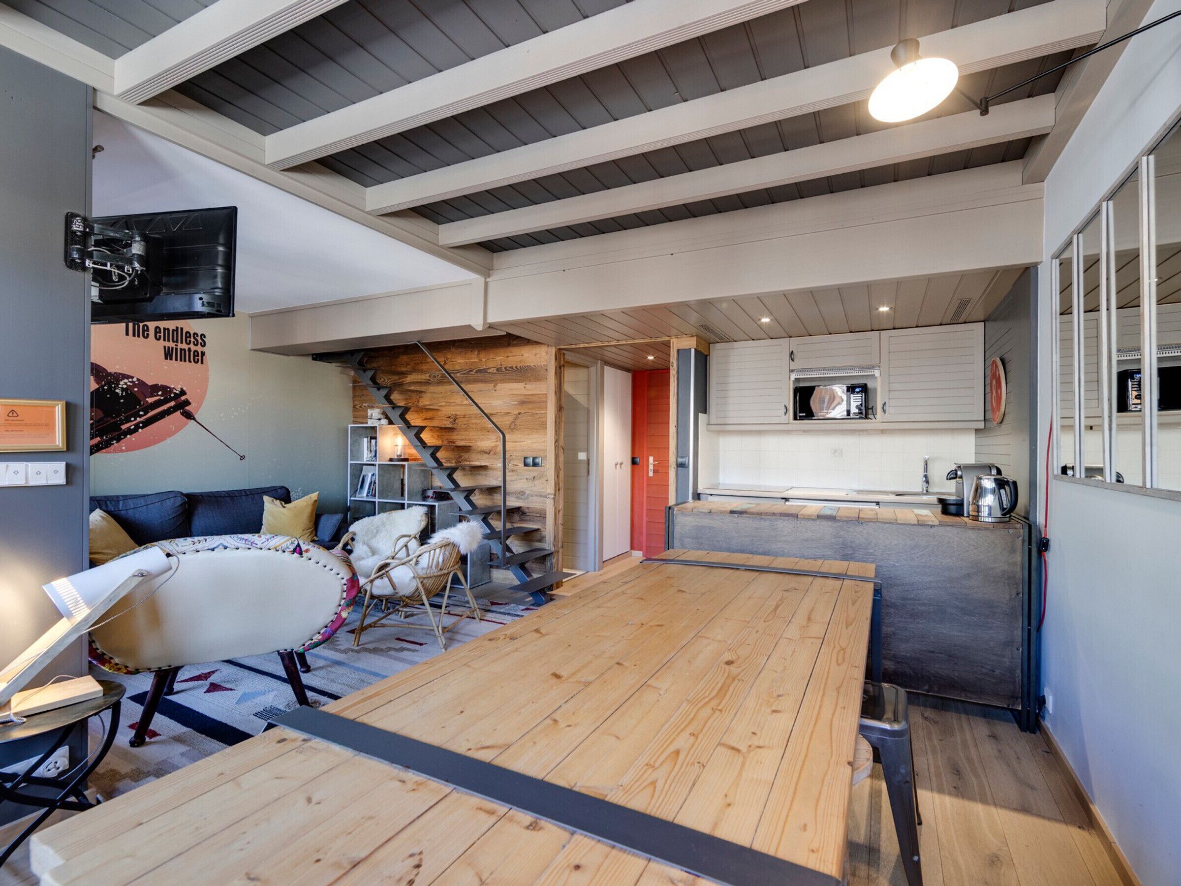 Un interior moderno con una mesa de comedor de madera, un sofá, una silla, una escalera y una zona de cocina.