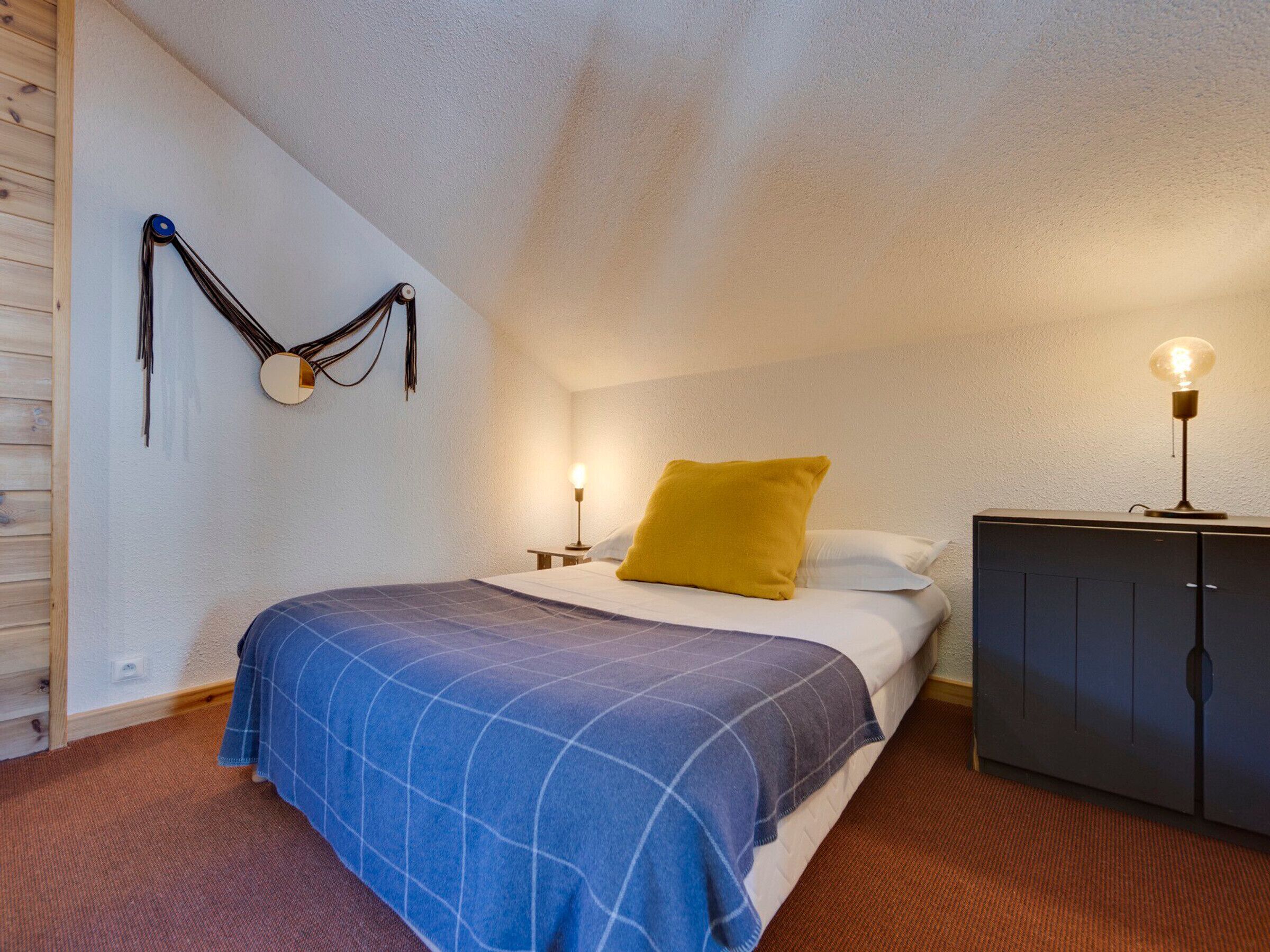 A bedroom with a bed, a nightstand, a lamp, a wardrobe, and a wall-mounted light fixture.
