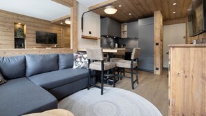A modern interior with a grey sofa, dining table, and chairs, wooden beams, and a kitchen area. - Renovated apartment at the slopes - 4 guests (Val-d'Isère)