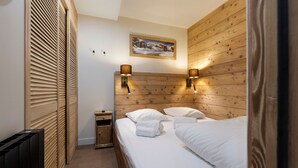 A hotel room with a wooden headboard, two bedside lamps, a painting above the bed, a small bedside table, and a radiator. - Renovated apartment at the slopes - 4 guests (Val-d'Isère)