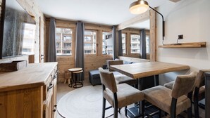 A modern interior with wooden walls, a round dining table, and a large window offering a view of the city. - Renovated apartment at the slopes - 4 guests (Val-d'Isère)
