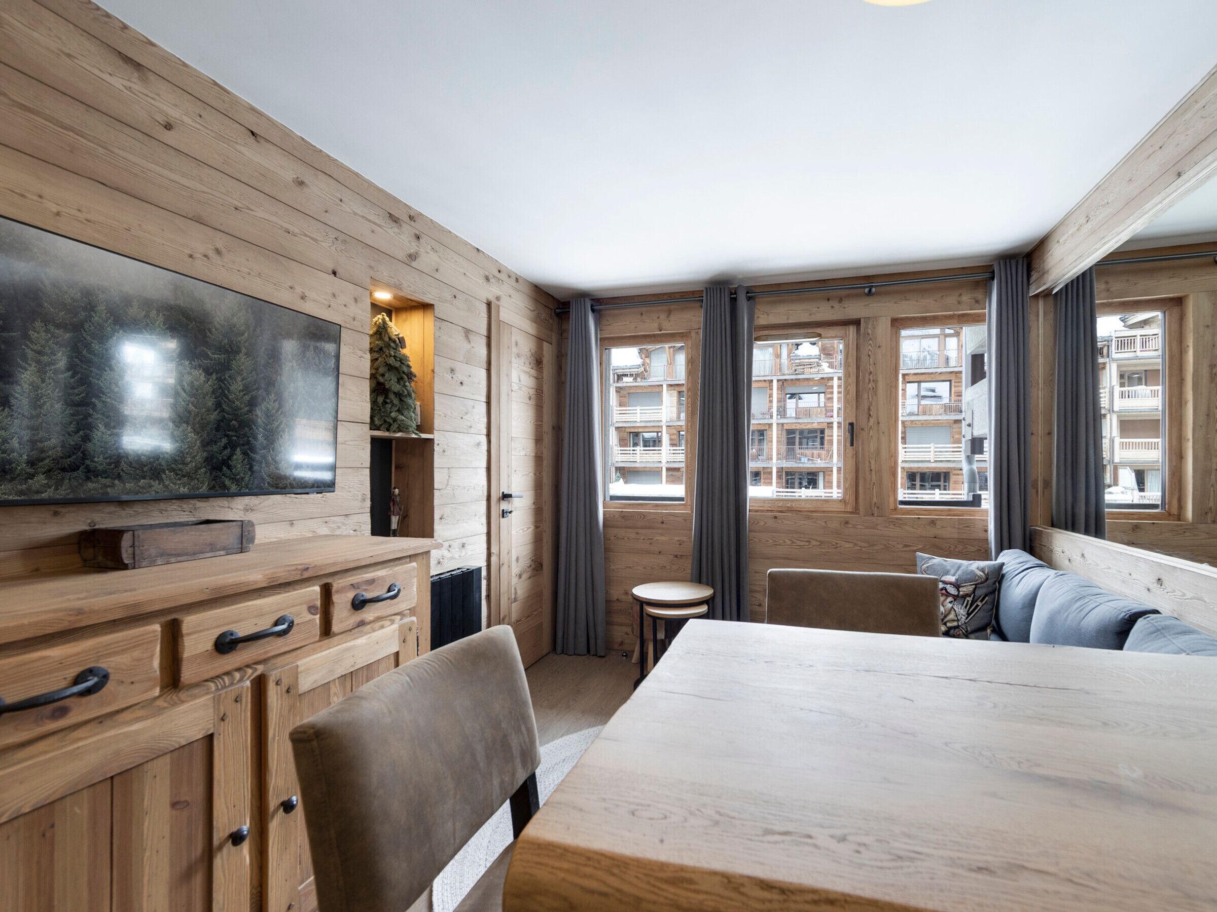Een houten interieur met een televisie, een eettafel en uitzicht op gebouwen.