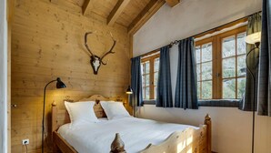 Une chambre à coucher dans une cabane en bois, avec un lit, un crâne de cerf accroché au mur et une fenêtre avec des rideaux.