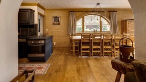 Une cuisine chaleureuse avec des meubles en bois, un coin repas comprenant une table et des chaises, et une grande fenêtre en arc de cercle qui laisse entrer la lumière naturelle.
