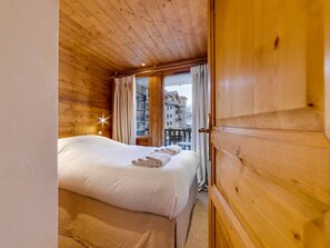 A wooden room with a bed, a window with curtains, and a view of buildings outside. - Bright apartment with parking - 4 guests (Val-d'Isère)