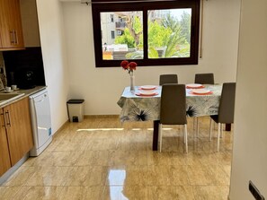 A compact kitchen with a dishwasher, a small trash bin, and a dining area with a table set for four.