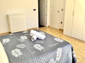 A neatly made bed with a grey quilt featuring white leaf patterns and the word 'Berigant' on it.