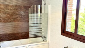 A bathroom with a bathtub, a shower, a window with a view, and a toilet.