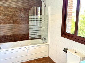 A bathroom with a bathtub, a shower, a window with a view, and a toilet.
